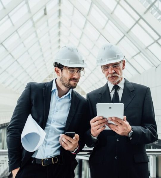 two-successful-entrepreneur-helmet-with-project-laptop-new-buildings-stay-near-glass-roof_496169-971